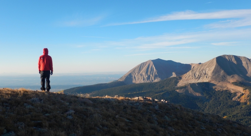 A person faces away from the camera overlooking a vast mountainous landscape.